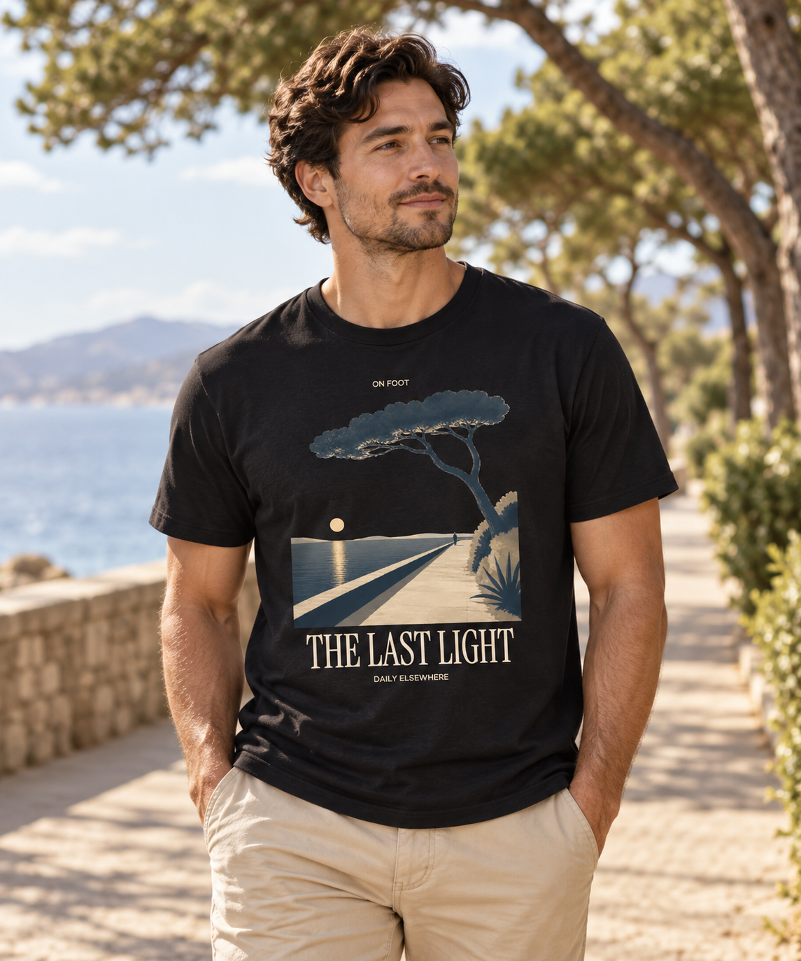 Male model wearing The Last Light black T-shirt with light coastal-path and tree artwork on the front.