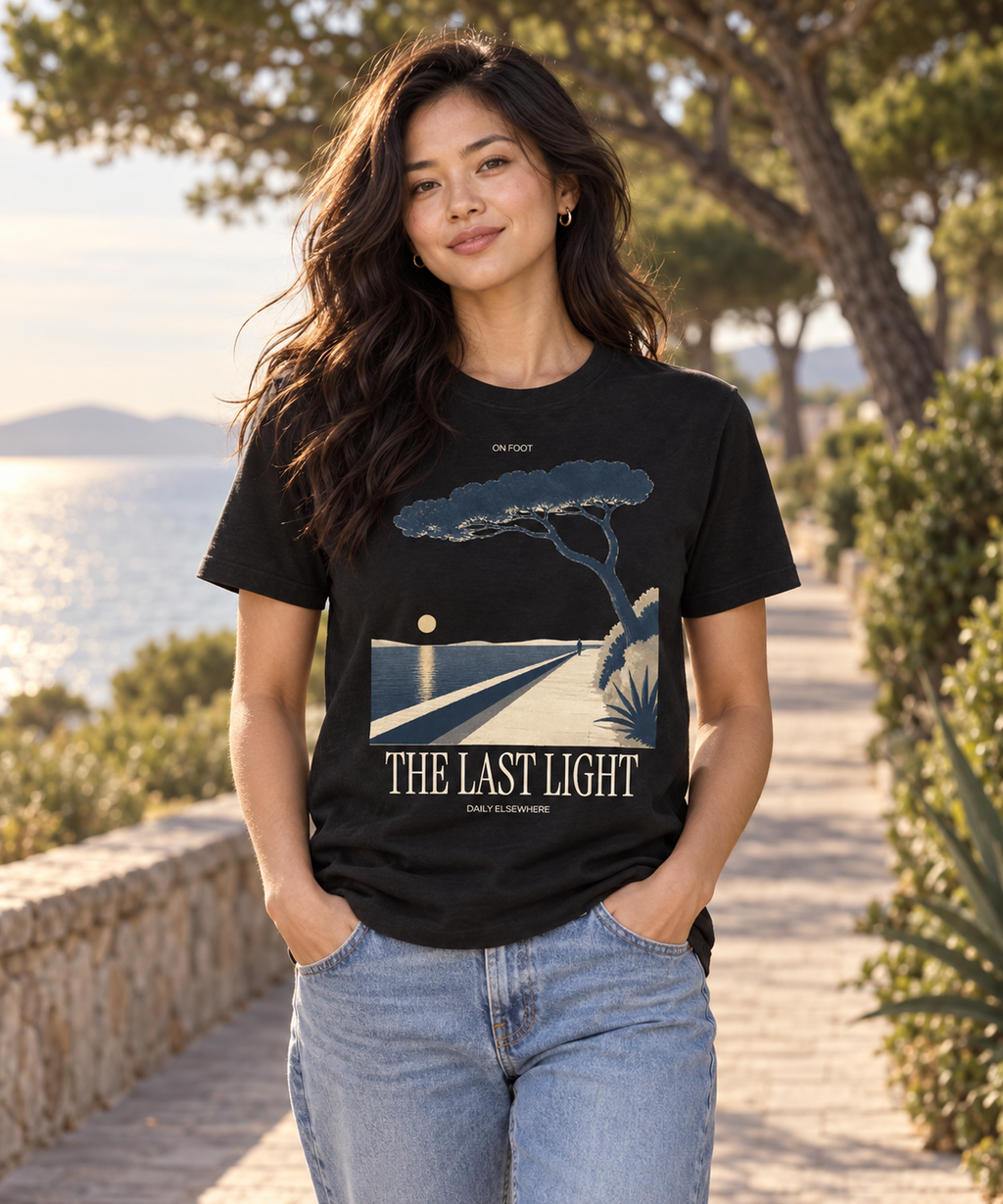 Female model wearing The Last Light black T-shirt with light coastal-path and tree artwork on the front.