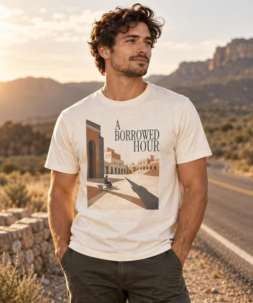 Male model wearing the A Borrowed Hour Natural Raw T-shirt with dark title lettering and sunlit courtyard artwork.
