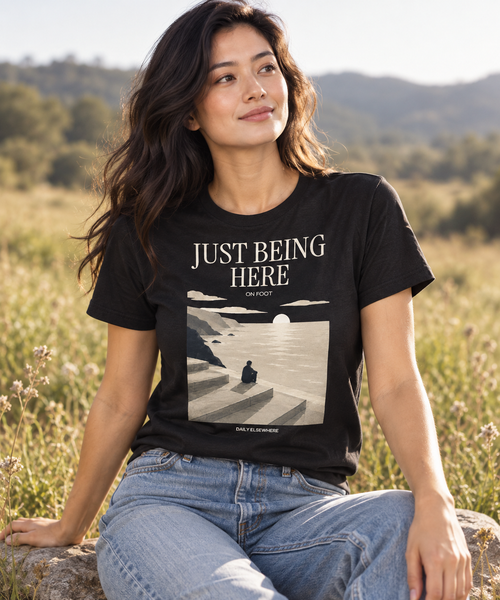 Just Being Here — Dark T-shirt with light front artwork on a contextual background. Daily Elsewhere.