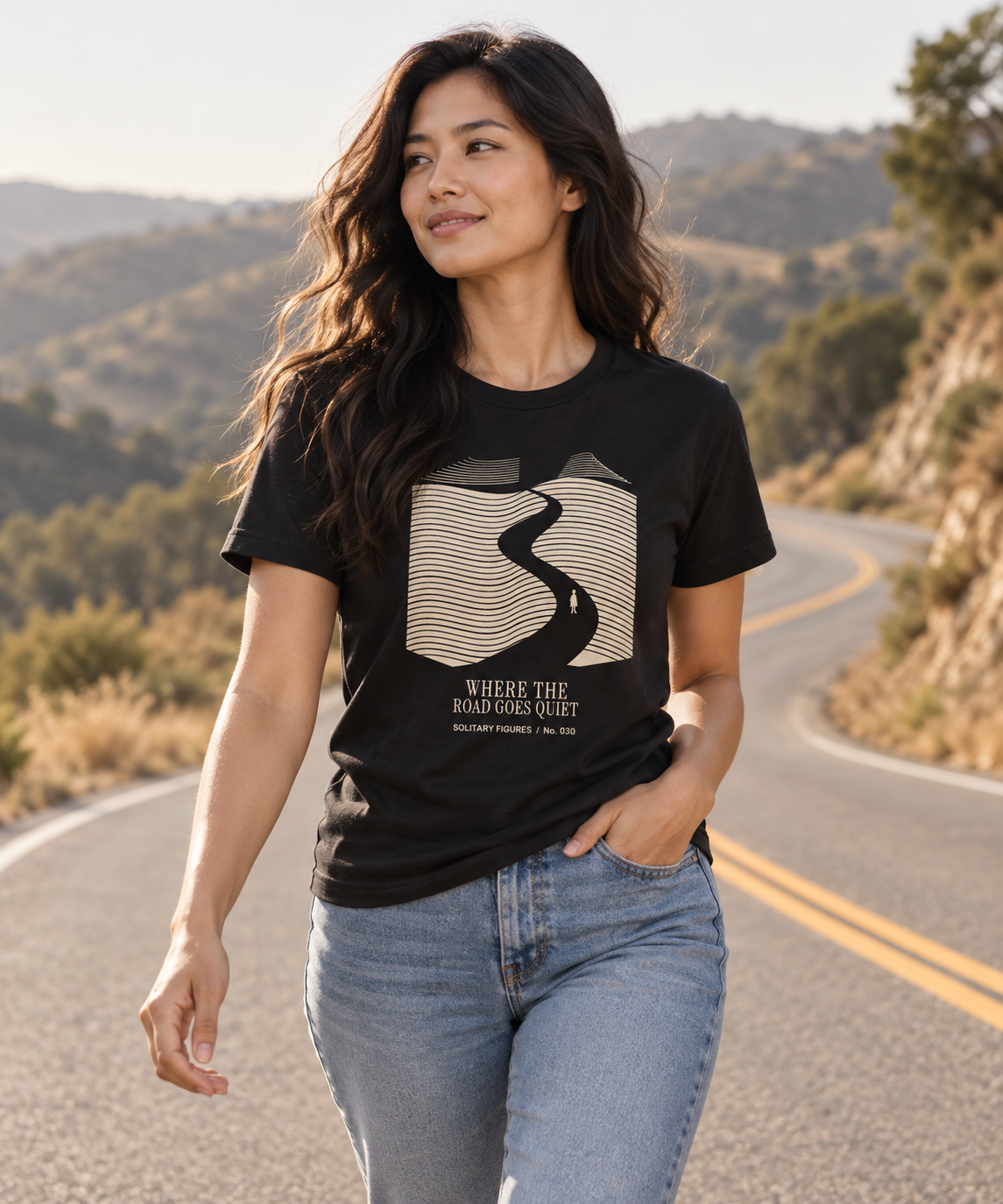 Where the Road Goes Quiet — Female model wearing a dark T-shirt with light front artwork. Daily Elsewhere.